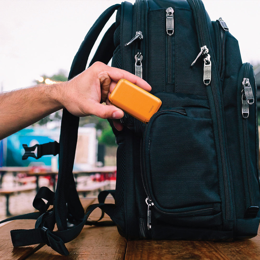 Person placing an ultra-slim 65W wall charger with leather design into a backpack on a wooden surface.