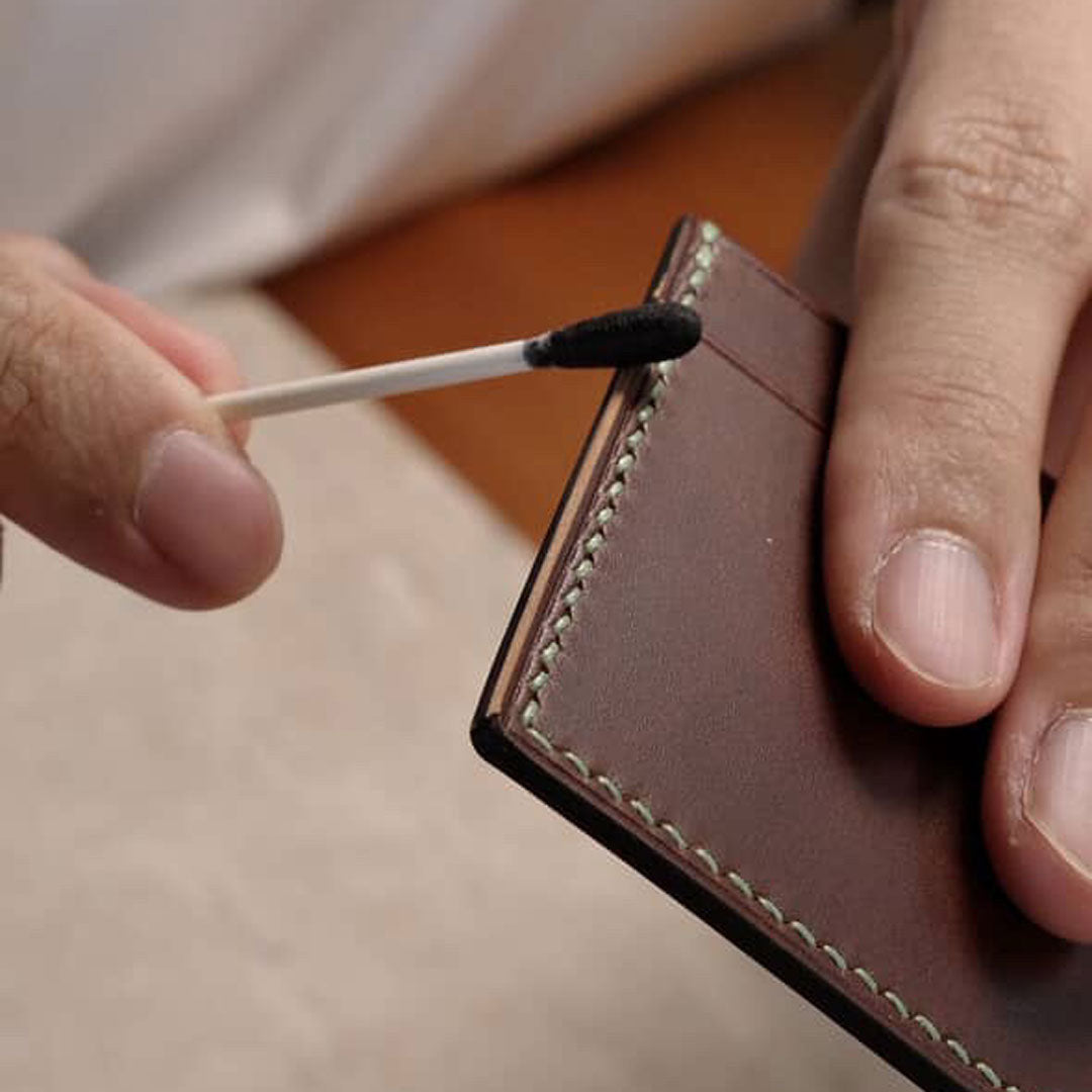 Person using a matchstick to dye a brown leather wallet's edge.