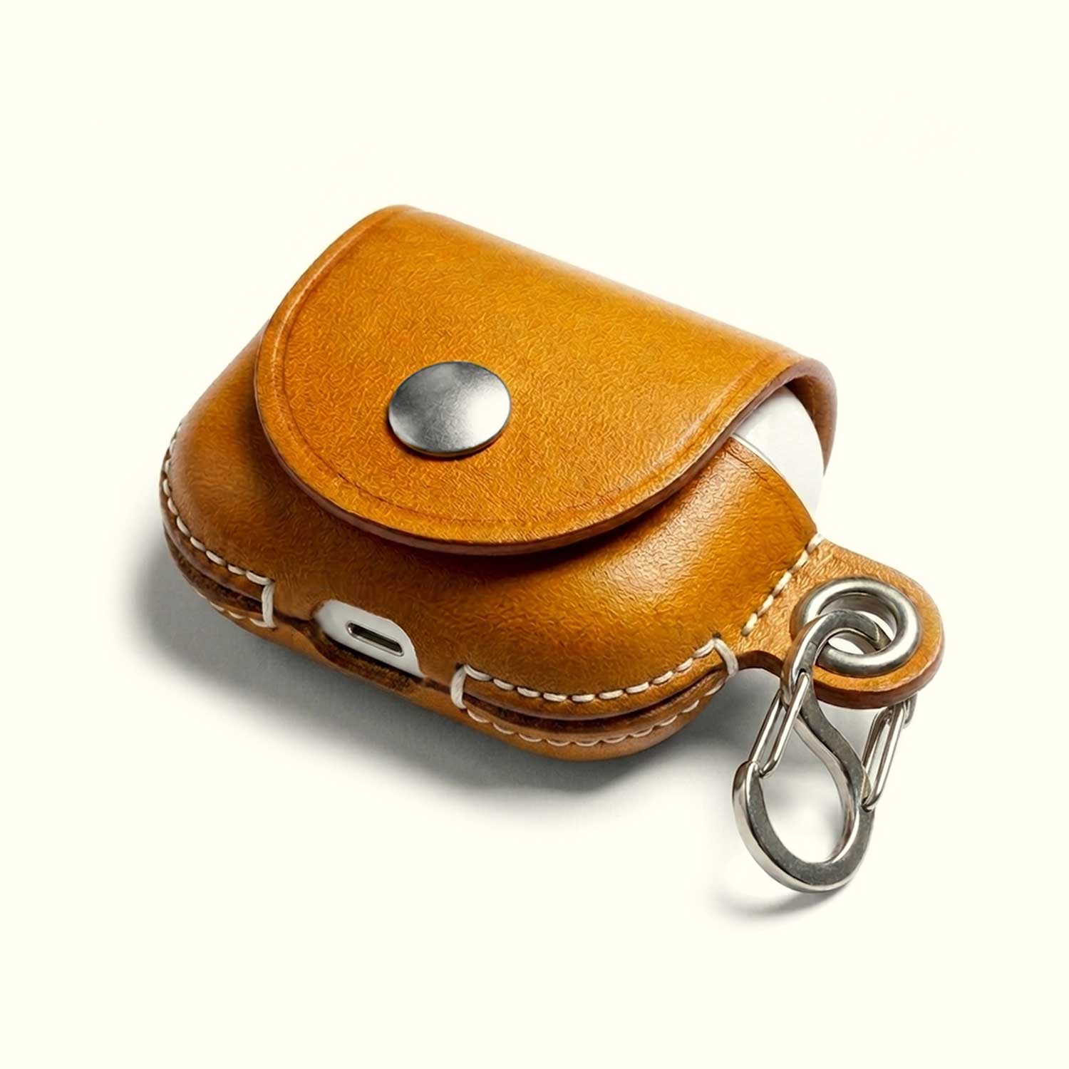 A tan leather AirPods case cover with a silver snap button and a silver carabiner clip, shown on a clean off-white background.