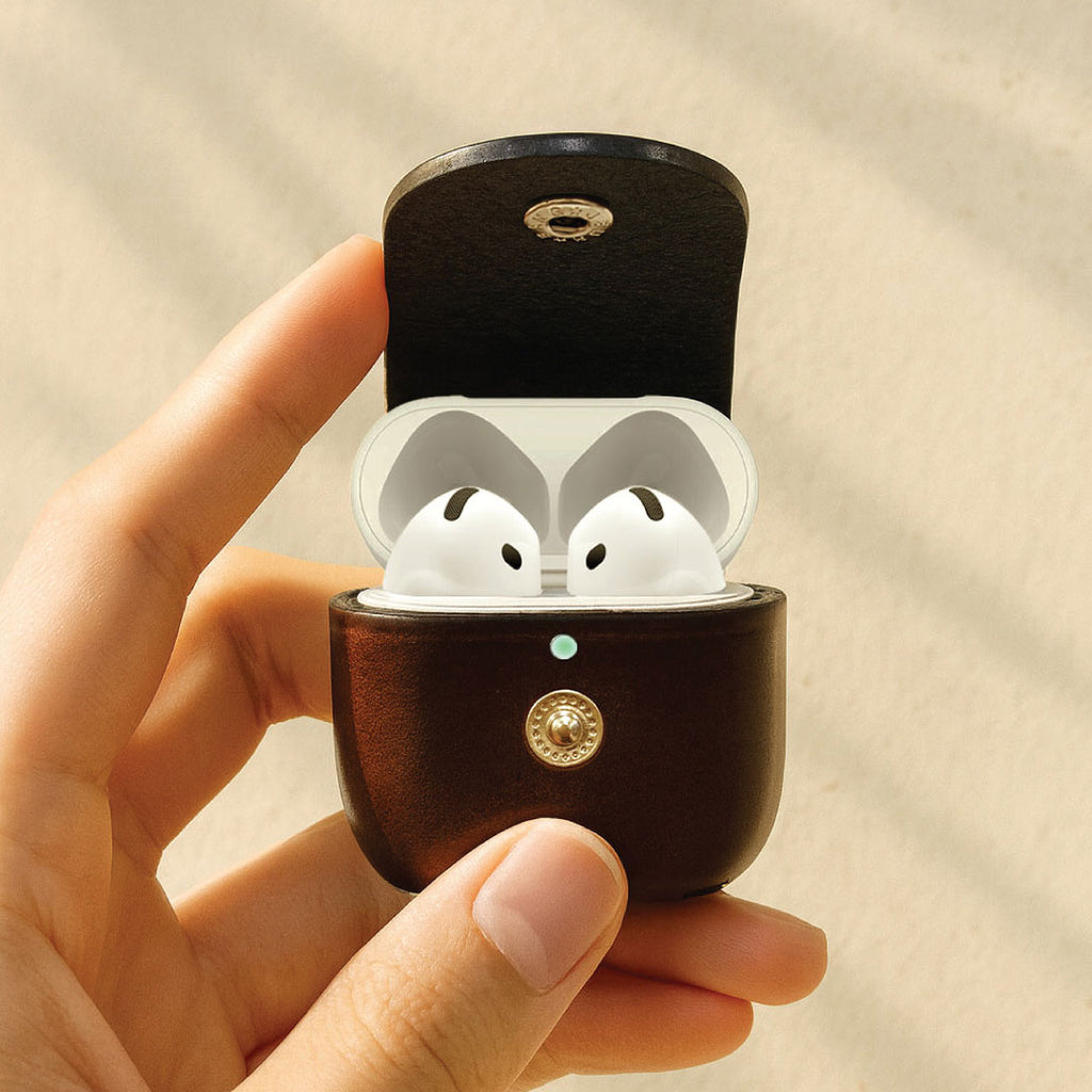 Wooden case with white wireless earbuds held by a hand against a beige background