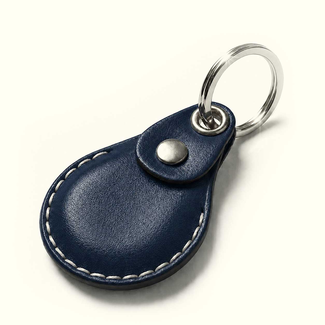 A navy blue leather keychain for AirTag with white contrast stitching and a silver metal key ring, shown on a light cream background.