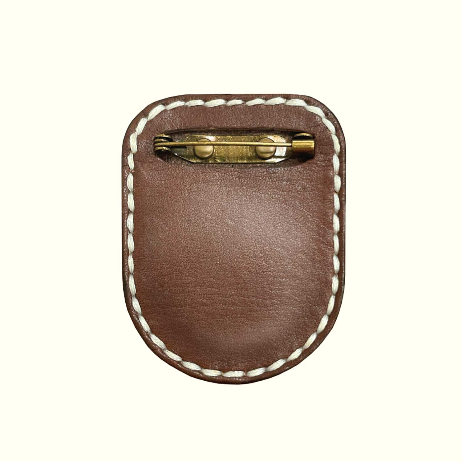 A brown leather brooch-pin holder for AirTag with white contrast stitching and a brass pin clasp