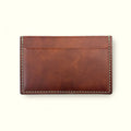 A brown leather card holder wallet with light-colored stitching, shown flat against a light cream background.