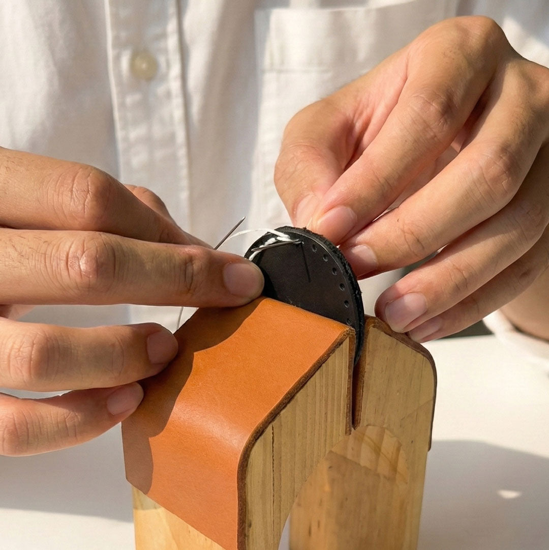 The craftsman is performing sandal stitching on the AirTag Case