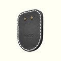 A black leather pouch for AirTag with white contrast stitching and two brass rivets, featuring the embossed brand name 'Vogue' on a light cream background.