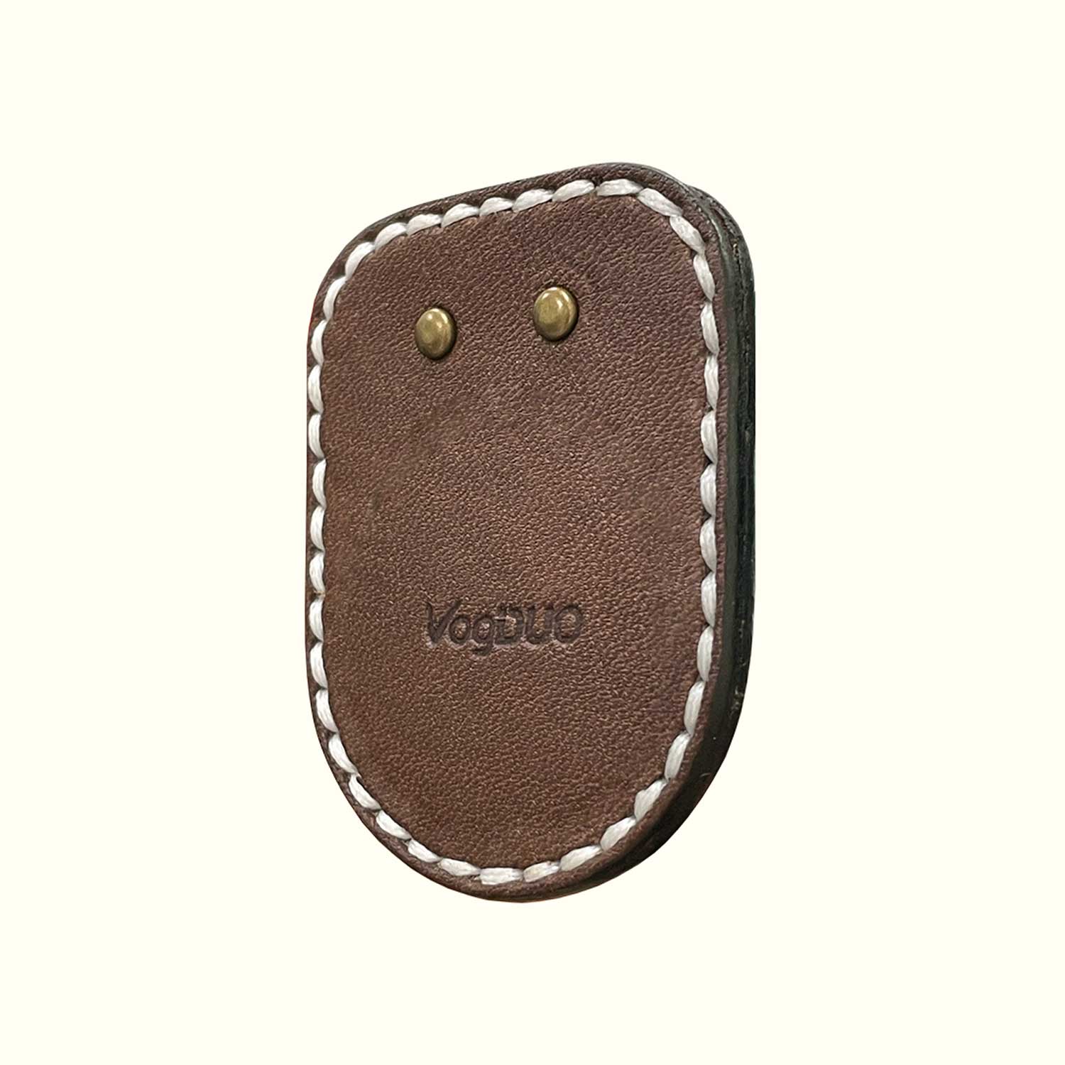 A brown leather case for AirTag with white stitching and brass rivets, featuring the embossed brand name 'VogDUO' on a light cream background.