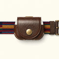 A close-up of a VagDUO belt-clip Case for AirPods Pro 3. The center features a brown leather case with a brass snap button and debossed brand name, flanked by a woven multicolor belt strap with navy, red, yellow, and blue stripes on a light cream background.
