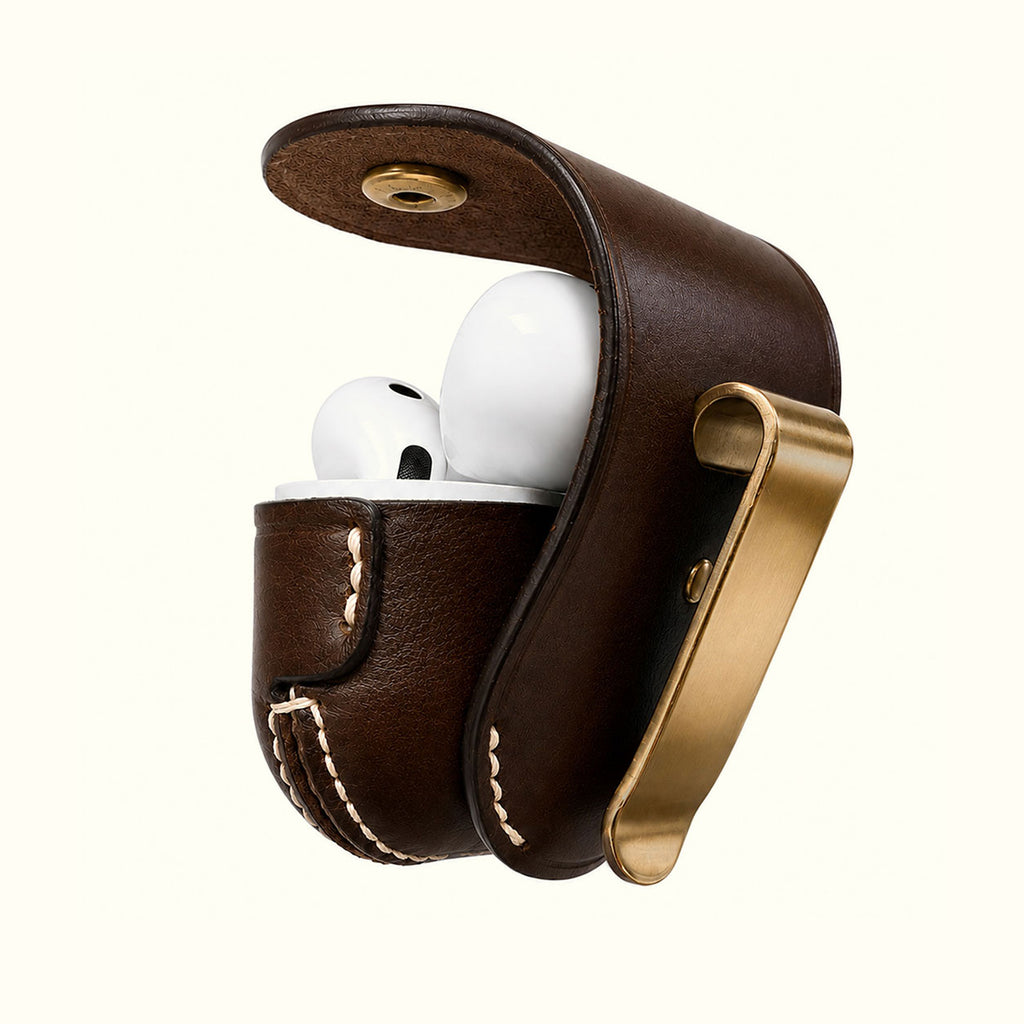 A dark brown leather AirPods Pro case with Brass clip and white stitching, shown open with white AirPods Pro 3 inside on a light cream background.