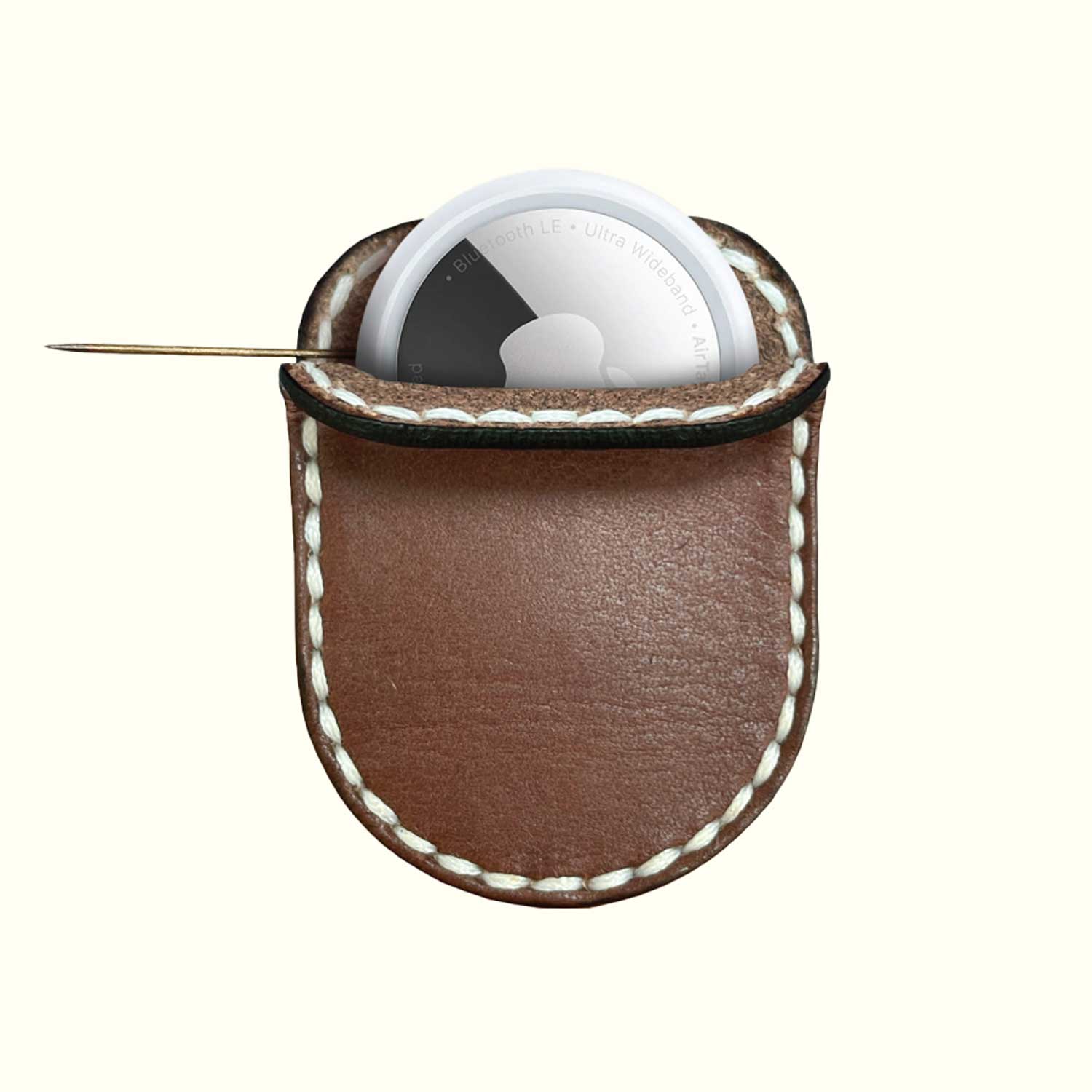 A brown leather case for AirTag with white contrast stitching, holding a white circular dial tool with a metal pin extending from the side