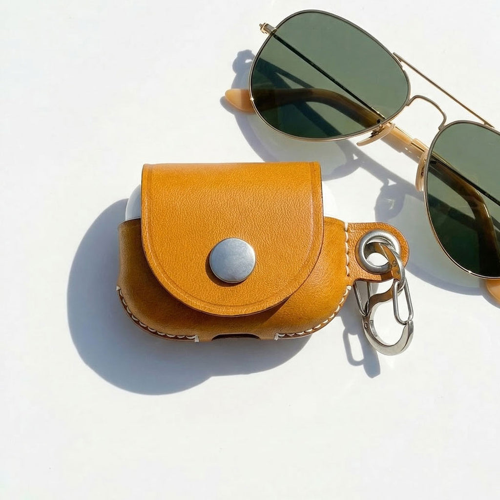 Tan leather pouch with a keychain for AirPods Pro and sunglasses on a white background