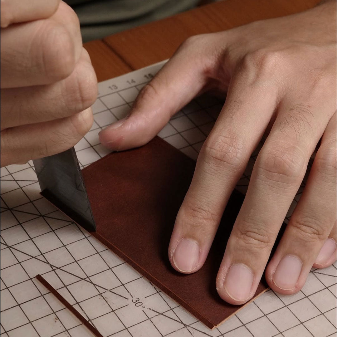 Person cutting brown leather using a traditional leather cutter.
