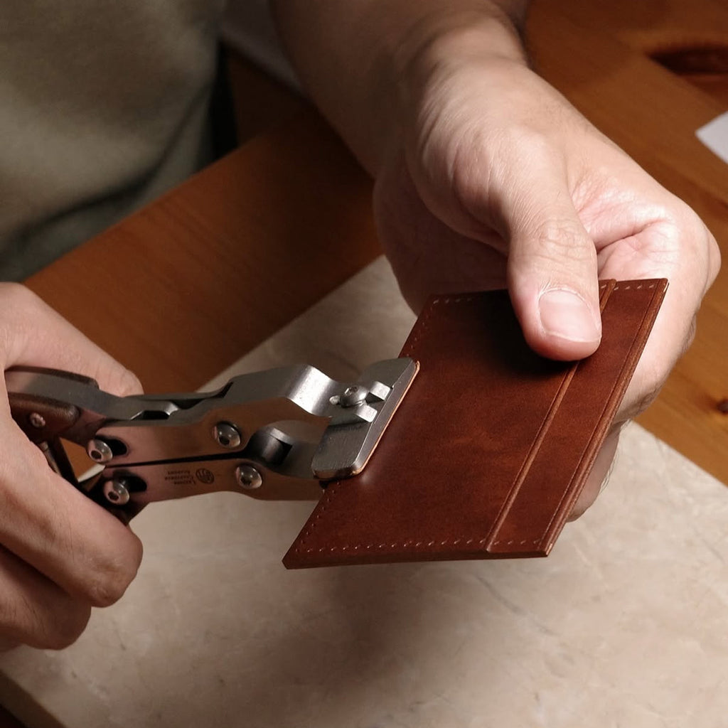 Person using a leather parallel clamps on a brown leather wallet to make sure the leather sticked to each other well.