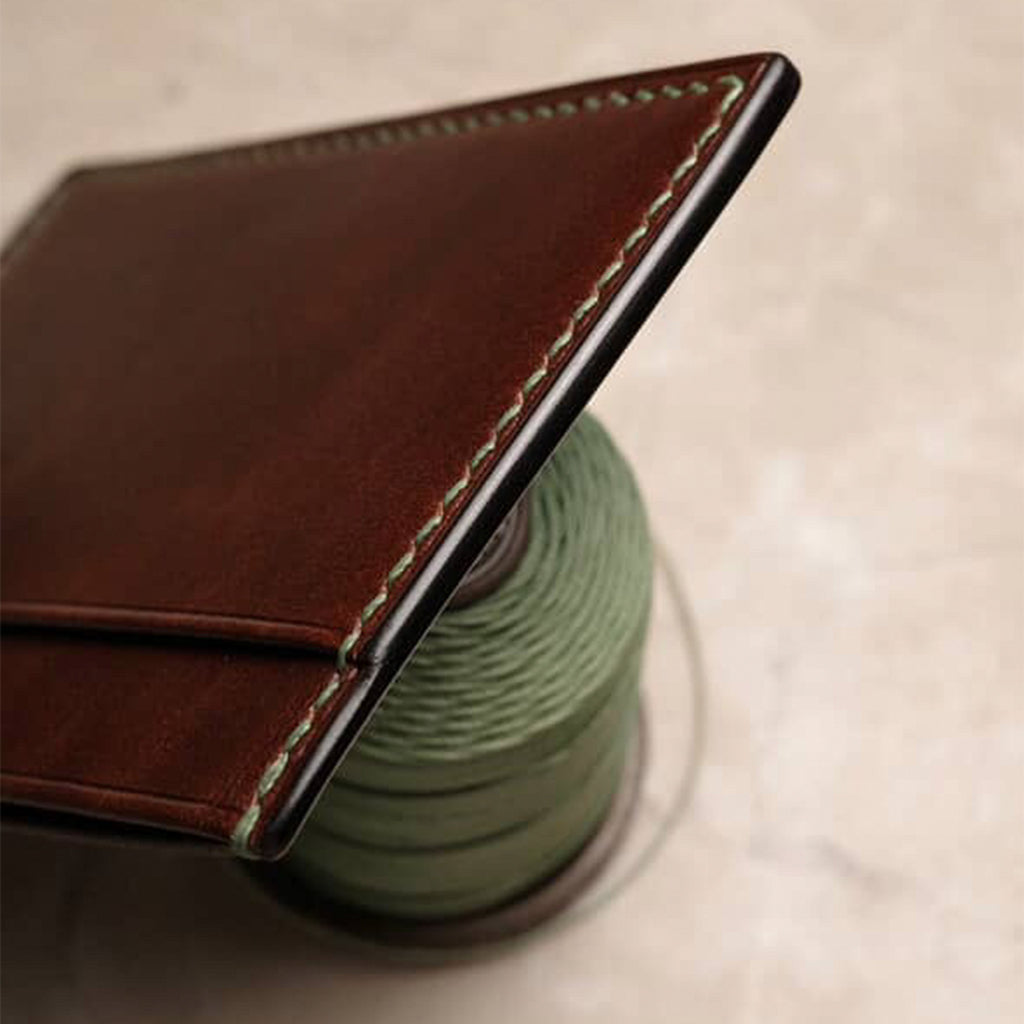 Brown leather wallet's polished edge shining after being carefully sanded on a spool of green thread