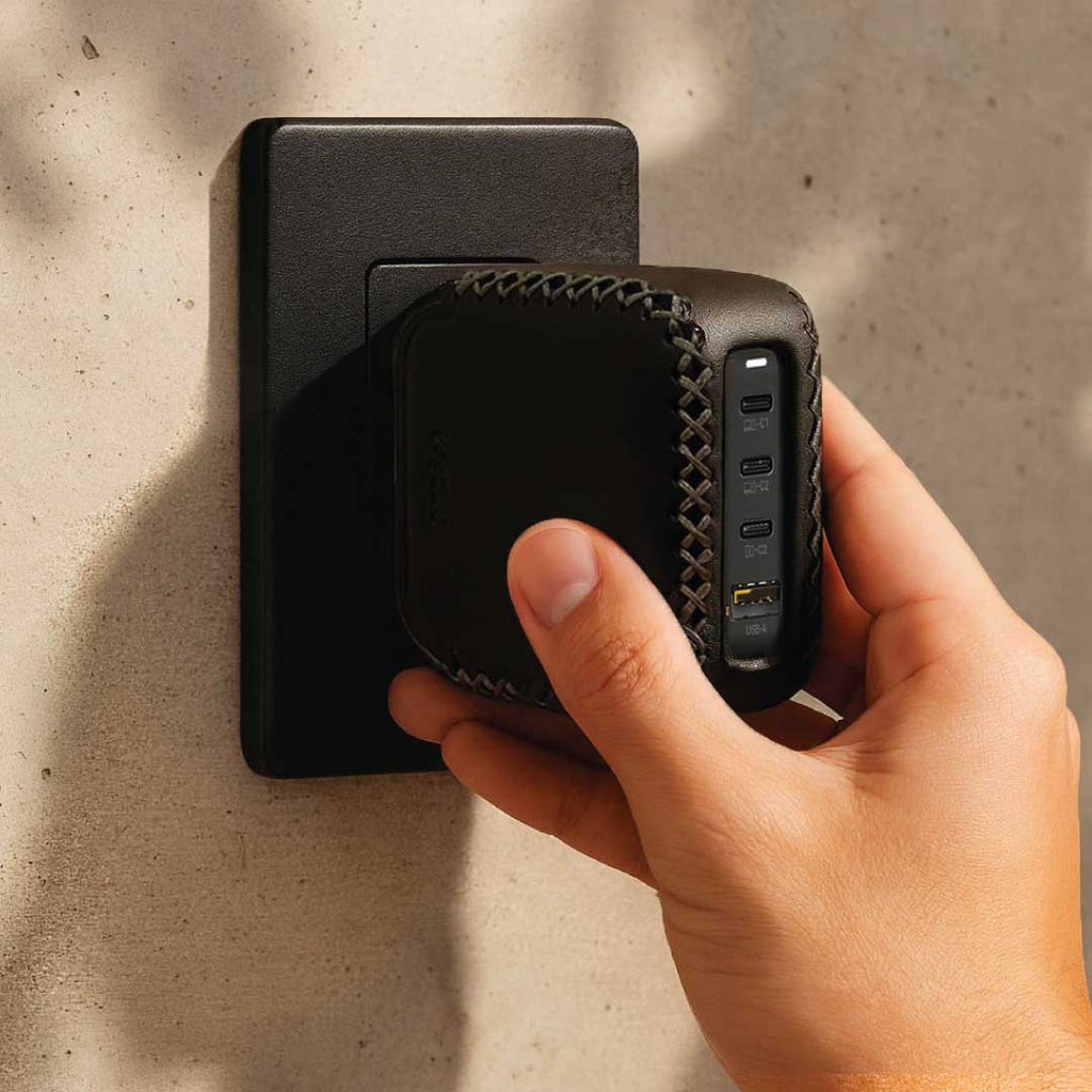 Hand holding a black power adapter with elegant leather design against, fits old money and comfortable lifestyle