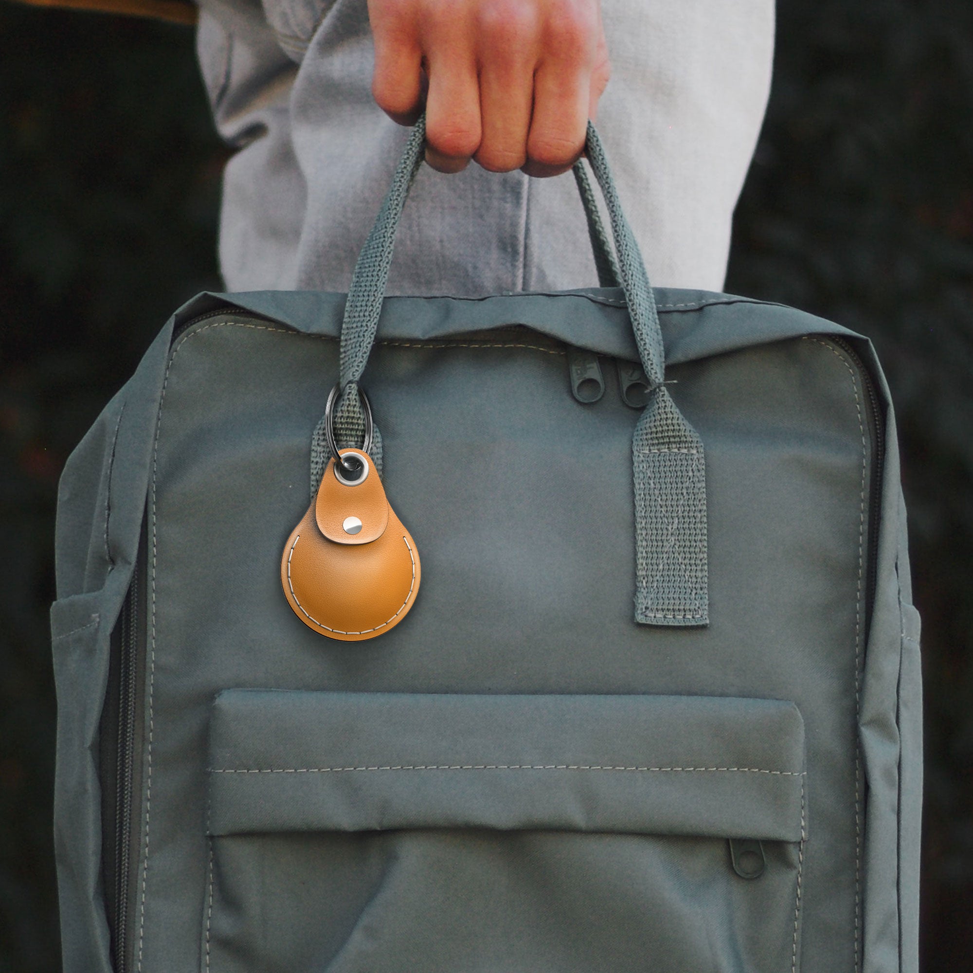 Person holding a green backpack with an AirTag leather case