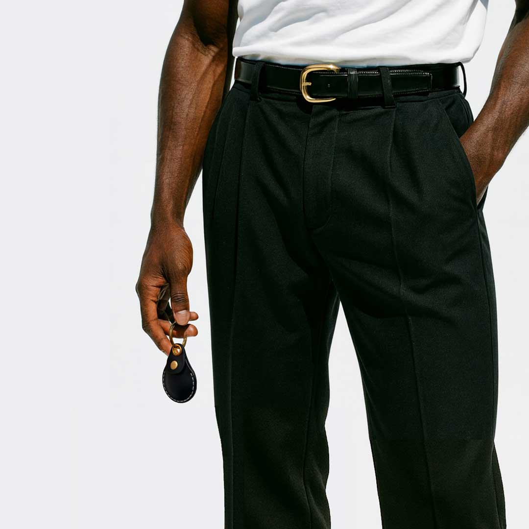 Person wearing black dress pants with a white shirt, casually carrying a VogDUO AirTag Leather case on his way home, showing stylish and confidence.