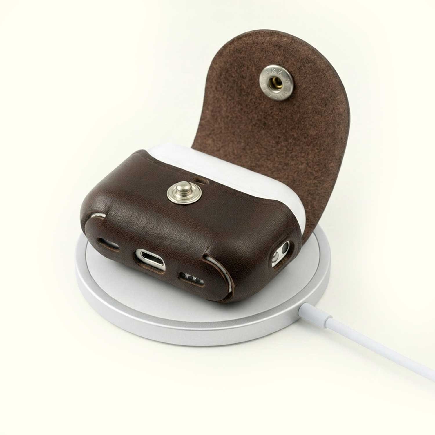 A brown leather AirPods Pro case standing open on a round white charging stand, with a wireless charging pad extending to the right on a clean off-white background.